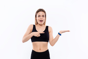 Fototapeta na wymiar Young sporty blond woman in a black sportswear with smart watches for pulse measuring pointing with one hand at the pulm of a hand