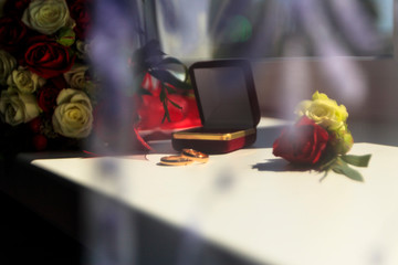 daylight. on the window are wedding rings. there are flowers that are red and white roses.
