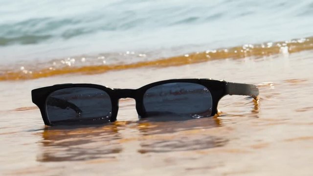 Sunglasses on beach. Sea waves, sunny day. Concept of holiday, vacation, relaxation, day at seaside