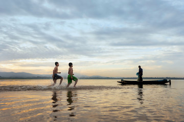 Fototapeta premium Children fishermen still cast fishing villages.Son fishing swimming and fishing equipment. happy the smiles of the children.The fishermen will cast On the old wooden boat A beautiful morning sunrise.