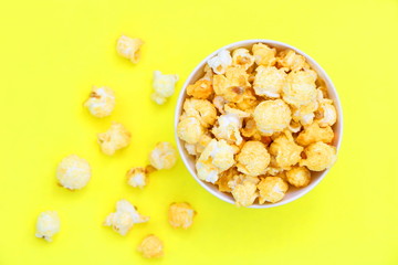 Top view isolated salted popcorn mix with cheese popcorn spilled from white bowl on yellow table background, movie cinema time concept
