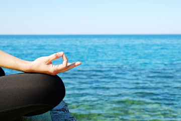 Fototapeta na wymiar Attractive sporty young yogi woman wearing sportswear practicing yoga, sitting in padmasana lotus pose, meditating on cliff over the calm ocean background. Close up, copy space.