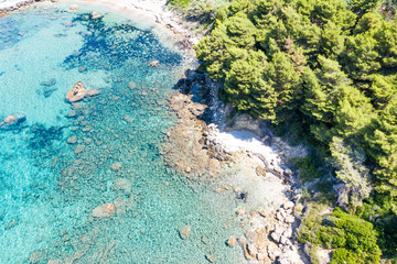 Aerial view of green seashore and turquoise sea water. Island with green trees in the ocean seen form above.