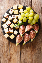 Mediterranean antipasti appetizer of cheese, fresh grapes and figs close-up on a slate board. Vertical top view