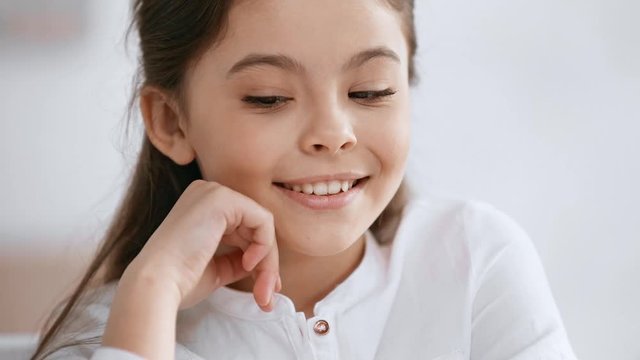 front view of cute preteen child smiling at camera, propping face with hand and looking around