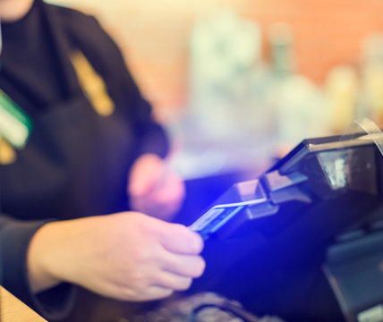blurry image of the cashier is swiping the credit card or member card at the card reader with the cash register machine in the store. Saleswoman receiving payment from customer in store.