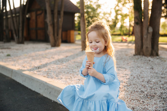 Beautiful little girl in a blue dress eating an ice cream