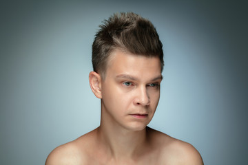 Portrait of shirtless young man isolated on grey studio background. Caucasian healthy male model looking at side and posing. Concept of men's health and beauty, self-care, body and skin care.