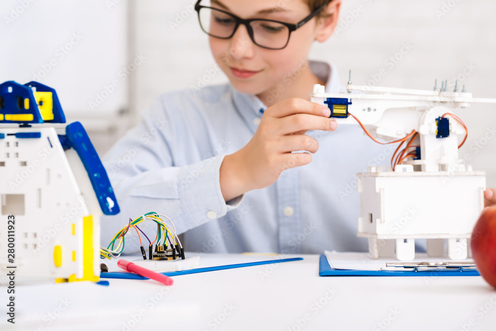 Poster concentrated boy constructing robot at class, closeup