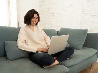 Happy young woman working on her laptop sitting cross-legged on the sofa. In technology concept