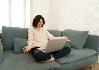 Happy young woman working on her laptop sitting cross-legged on the sofa. In technology concept