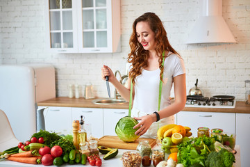 Young happy woman cutting cabbage for making salad in the beautiful kitchen with green fresh ingredients indoors. Healthy food and Dieting concept. Loosing Weight