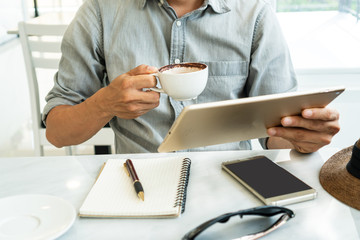 Businessman hold a cup of coffee while using tablet in a cafe.
