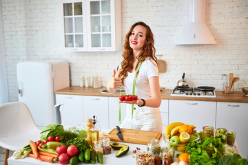 Young happy woman holding tomatoes for making salad in the beautiful kitchen with green fresh ingredients indoors. Healthy food and Dieting concept. Loosing Weight