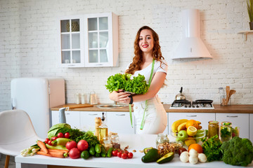 Young happy woman holding lettuce leaves for making salad in the beautiful kitchen with green fresh ingredients indoors. Healthy food and Dieting concept. Loosing Weight