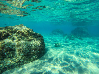 Underwater view of the rocks, sand and stones. The sandy and rocky bottom of the sea with some sun rays.