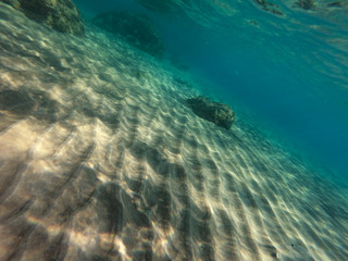 Underwater view of the rocks, sand and stones. The sandy and rocky bottom of the sea with some sun rays.