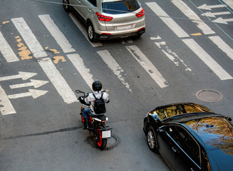 Motorcyclist and black and gray cars are at a pedestrian crossing at a traffic light during a traffic jam