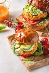 Vegan burger with carrot and avocado in classic bun, served on crumpled paper with avocado sauce and ingredients above on white marble table. Homemade healthy fast food.