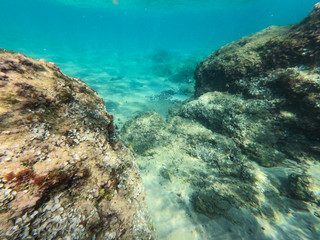 Underwater view of the rocks, sand and stones. The sandy and rocky bottom of the sea with some sun rays.