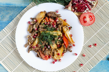 baked beef with vegetables and greens on a white plate blue background