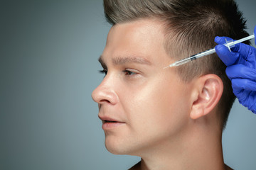 Close-up portrait of young man isolated on grey studio background. Filling surgery procedure. Concept of men's health and beauty, cosmetology, self-care, body and skin care. Anti-aging.