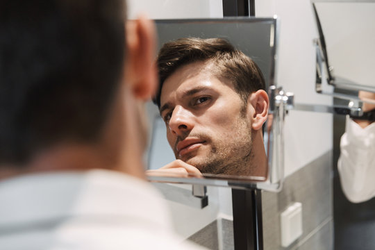 Image closeup of unshaved man looking at mirror in bathroom at hotel room during business trip