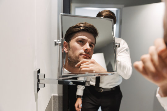 Image closeup of attractive man looking at mirror in bathroom at hotel room during business trip