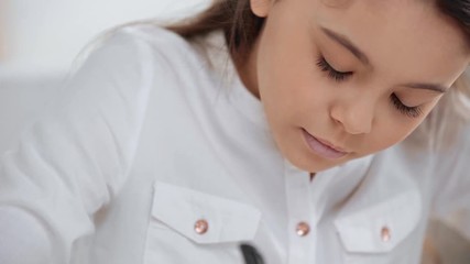focused schoolgirl in white shirt blinking while writing in copy book