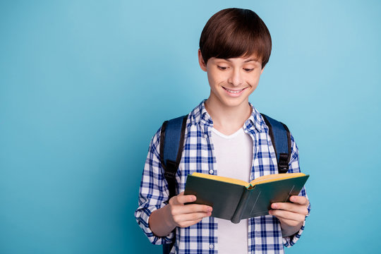 Portrait of pretty boy holding printed textbook wearing checked plaid shirt isolated over blue background