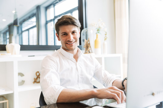 Image of smiling businesslike man sitting at table and working on computer in office