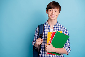Portrait of lovely student holding note books wearing checked shirt isolated over blue background
