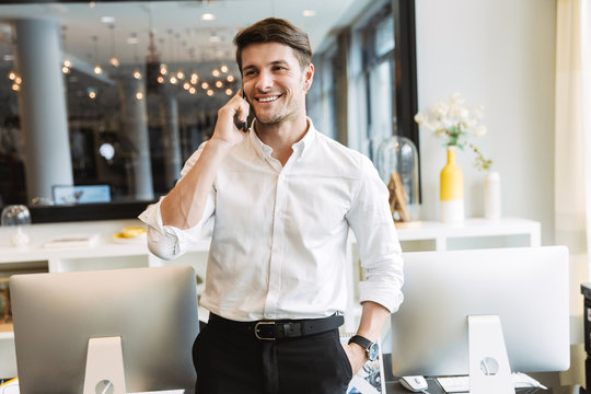 Image of beautiful businesslike man talking on cellphone while working in office