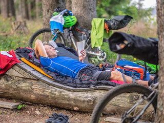 Mountain biker resting on a log reading book amidst woods, Baden-Württemberg, Germany
