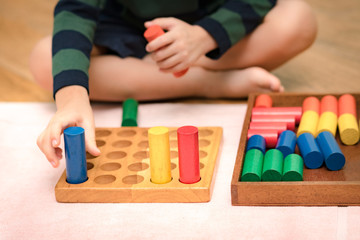 Closeup: Hands of a little Montessori kid (3-6) learning about size, orders, sorting, arranging by engaged colorful wooden sensorial blocks. Educational toys, Cognitive skills, Montessori activity.