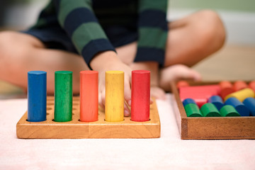 Fototapeta premium Closeup: Hands of a little Montessori kid (3-6) learning about size, orders, sorting, arranging by engaged colorful wooden sensorial blocks. Educational toys, Cognitive skills, Montessori activity.