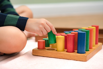 Closeup: Hands of a little Montessori kid (3-6) learning about size, orders, sorting, arranging by engaged colorful wooden sensorial blocks. Educational toys, Cognitive skills, Montessori activity.