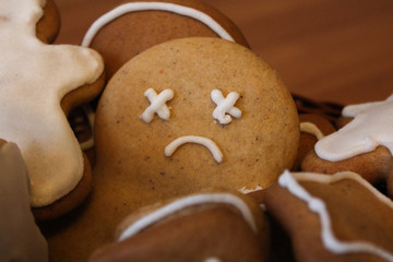 Homemade gingerbread men in the woven basket on the wooden table. Depressed christmas cookie with sad face covered with icing. New Year pastry in the shape of stars and men. Winter background