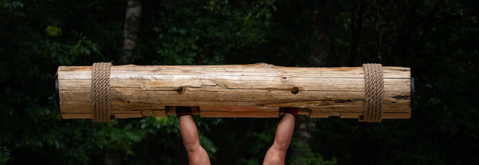 Strongest man in the world competition. Muscular hands lifting up heavy wooden trunk. Giant, mighty man lifting wood log at competition