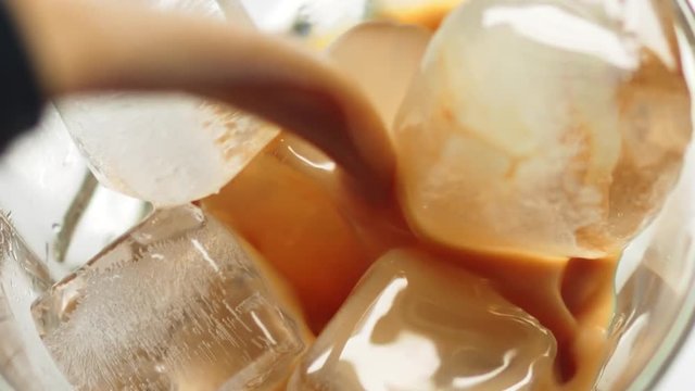 Pouring Irish cream whiskey beverage into glass over ice cubes.
