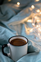 Coffee cup and garland on a bed. Atmospheric swedish hygge style. Cozy winter or autumn morning