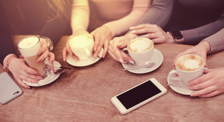 Four frmale friends sitting in a cozy cafe drinking coffee using smart phone with black isolated screen with place for text.