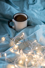 Coffee cup and garland on a bed. Atmospheric swedish hygge style. Cozy winter or autumn morning