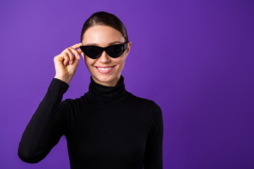 Close up photo of pretty woman touching her specs looking with toothy smile wearing black turtleneck isolated over violet purple background