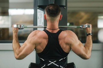 Fototapeta premium A young athlete trains in the gym. Shows the muscles of the back and chest. Back view