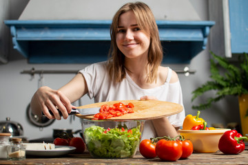 young girl prepares a vegetarian salad in the kitchen, she adds sliced ingredients to the plate, the process of preparing healthy food