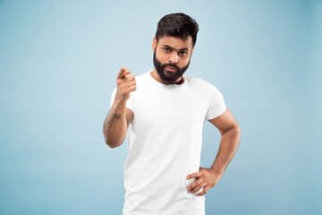 Naklejka premium Do połowy długości bliska portret młodego mężczyzny hindusów w białej koszuli na niebieskim tle. Ludzkie emocje, wyraz twarzy, koncepcja reklamy. Negatywna przestrzeń. Pokazywanie pustego paska, wskazywanie, wybieranie, zapraszanie.