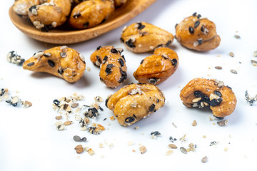 Sesame Coated Cashew Nuts on wooden spoon. Isolated on white background