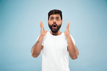 Half-length close up portrait of young hindoo man in white shirt on blue background. Human emotions, facial expression, ad concept. Negative space. Shocked, astonished or crazy happy feelings.