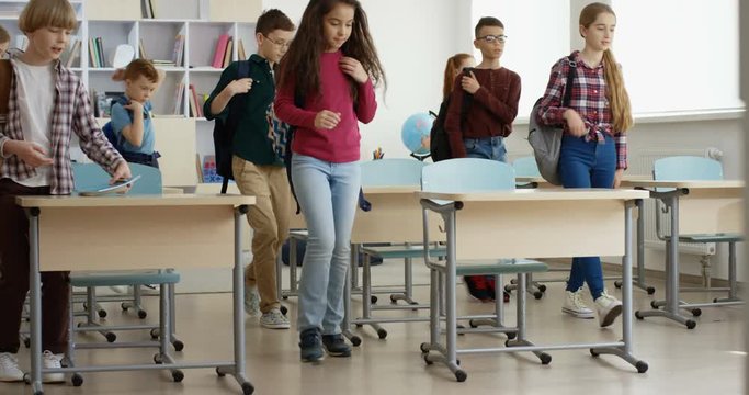 Teen Caucasian schoolchildren coming at the classroom, sitting at the desks and taking out textbooks and copybooks while preparing to the next lesson.